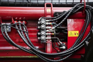 Bức ảnh nổi bật với hệ thống ống dẫn thủy lực chất lượng cao, được lắp ráp tinh gọn và khoa học trên nền máy móc công nghiệp màu đỏ đặc trưng. Các đầu nối, van điều khiển, khớp nối nhanh và đường ống bọc chống mài mòn thể hiện sự chính xác và an toàn trong thiết kế – tiêu chuẩn mà Thủy Lực Đại Dương